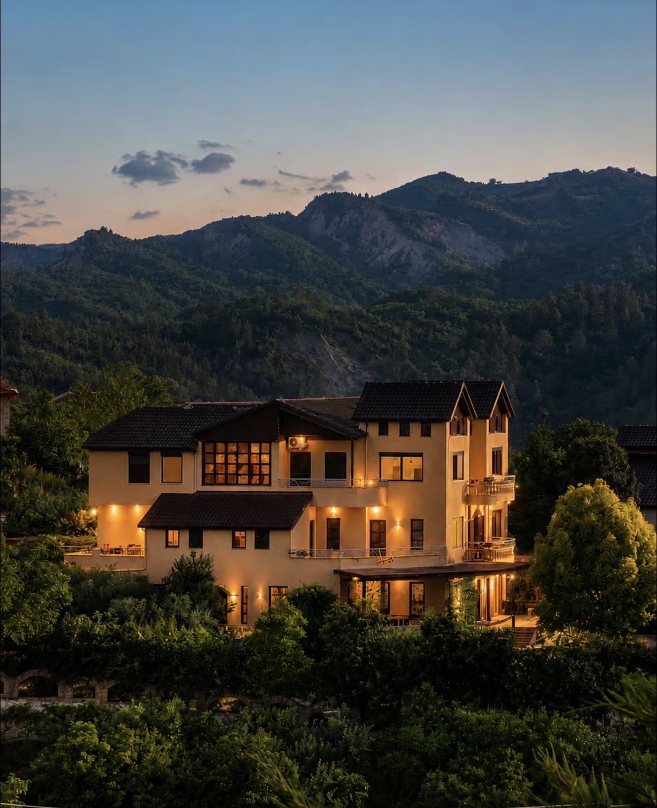 The villa at dusk, every window warm.